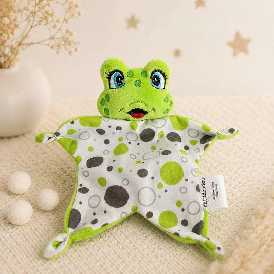 Mini doudou plat grenouille verte 16 cm avec lange à pois pour bébé, posé sur un plaid beige