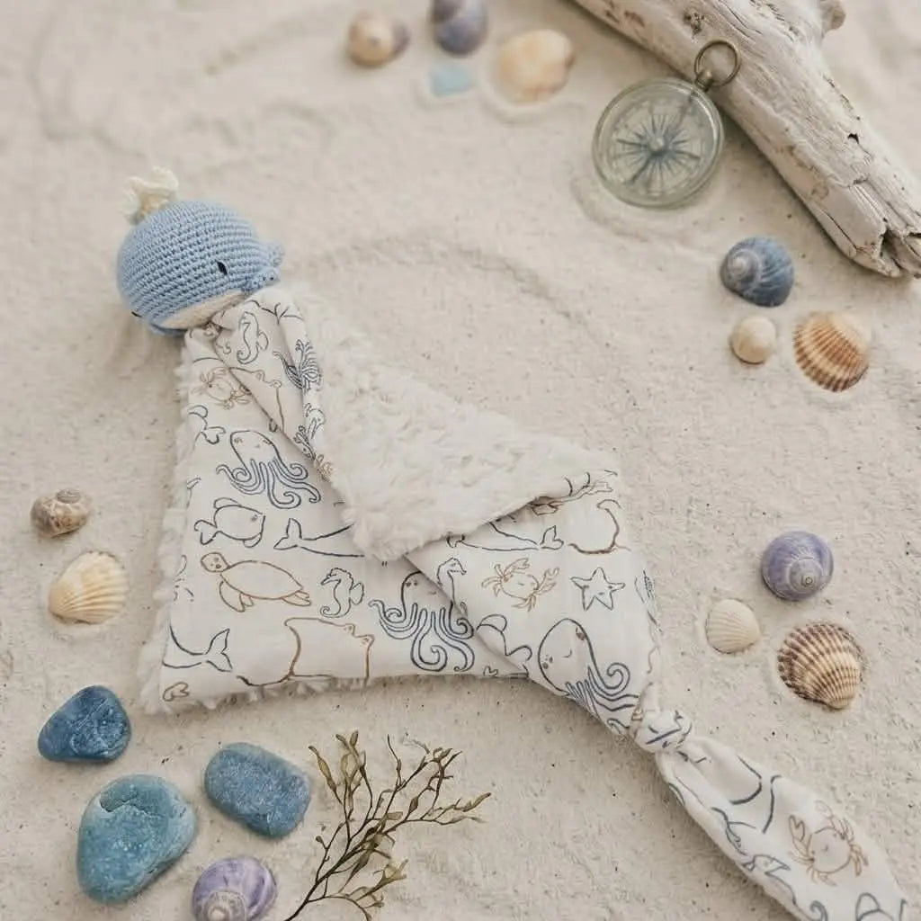 Doudou bébé baleine au crochet posé sur sable avec coquillages – cadeau de naissance