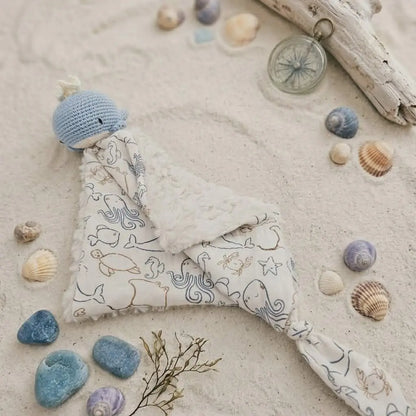 Doudou bébé baleine au crochet posé sur sable avec coquillages – cadeau de naissance