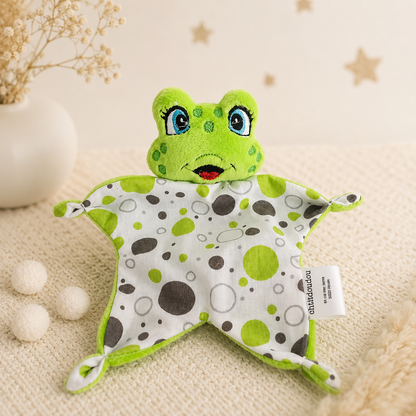 Mini doudou plat grenouille verte 16 cm avec lange à pois pour bébé, posé sur un plaid beige
