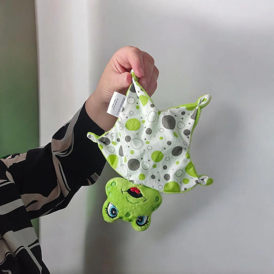 Mini doudou plat grenouille verte 16 cm avec lange à pois pour bébé, posé sur un plaid beige