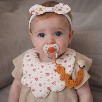 petite fille portant bandeau nœud, bavoir bandana floral et attache tétine crochetée