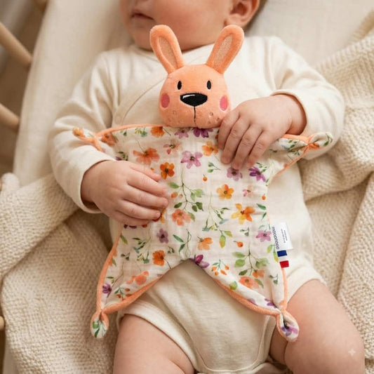 Bébé tenant un doudou plat lapin abricot chtitdoudou à motif floral aquarelle